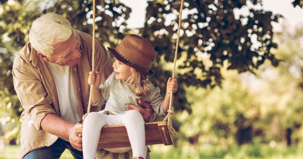 Grandfather pushes child on swing at park