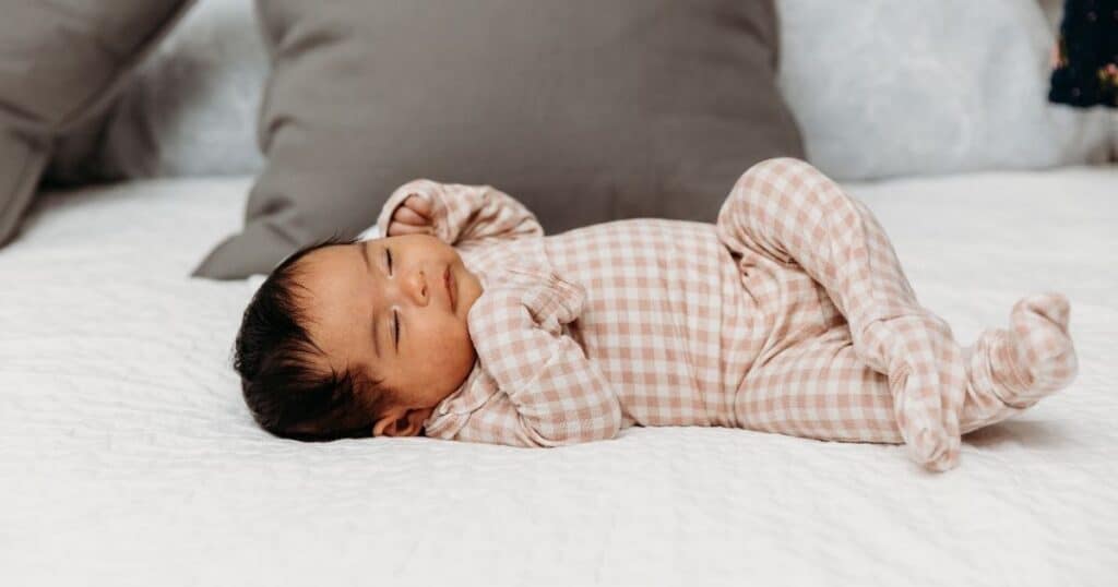 Newborn in plaid onesie sleeps on hedges with legs crossed
