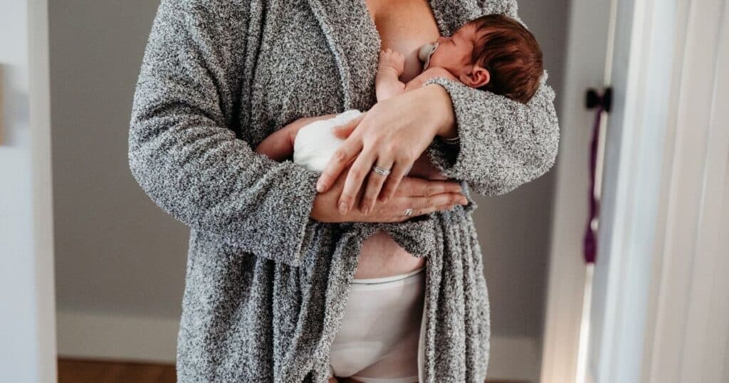 Mother in robe and disposable postpartum underwear cradles diapered baby in her arms