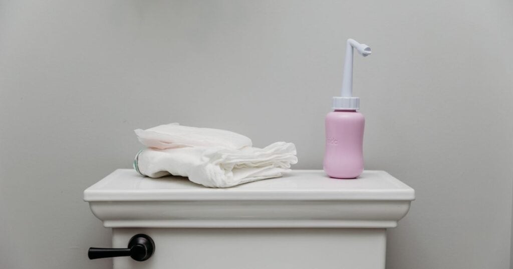 Postpartum underwear and peri bottle sit on top of a toilet