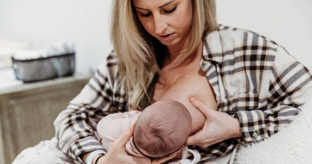 Mom puts baby to her breast while looking down in distress