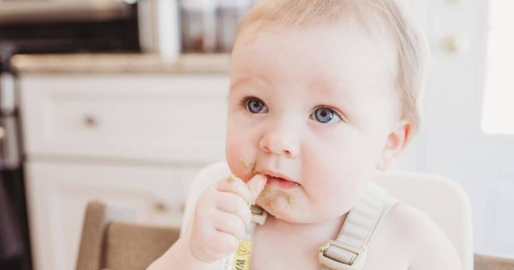 Toddler eats carrot with guacamole on it