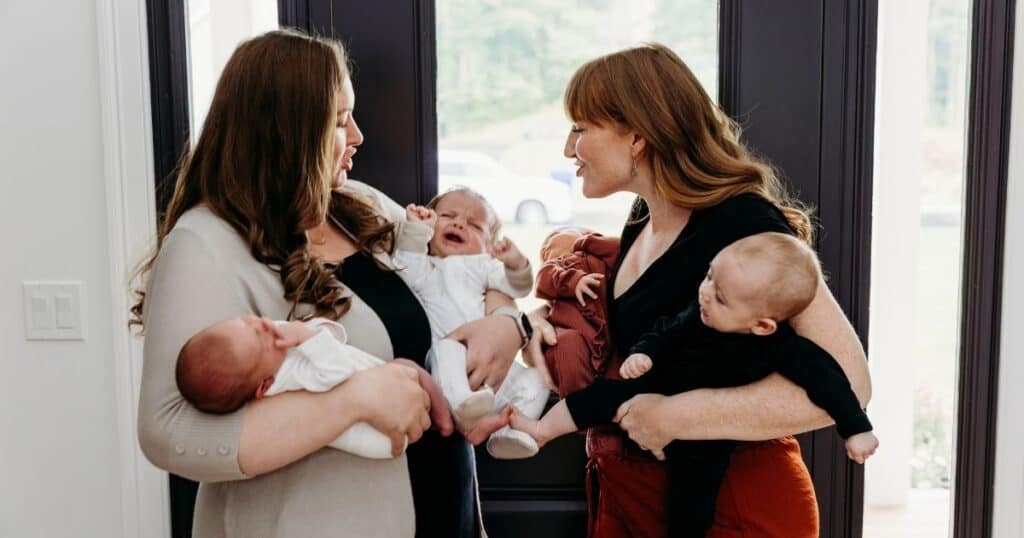 Two moms holding two babies each both shush a crying baby
