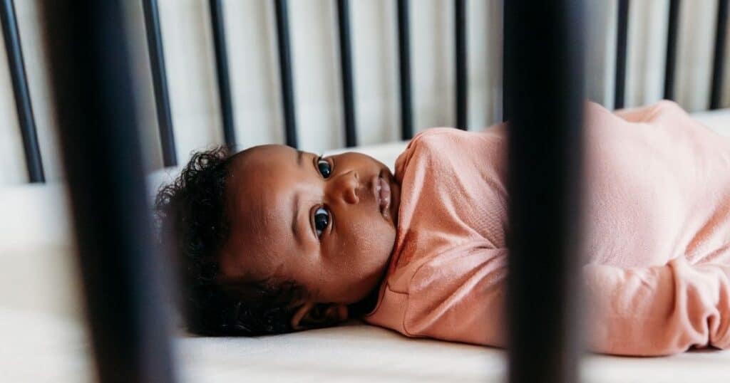 Baby awake in black crib wearing pink outfit