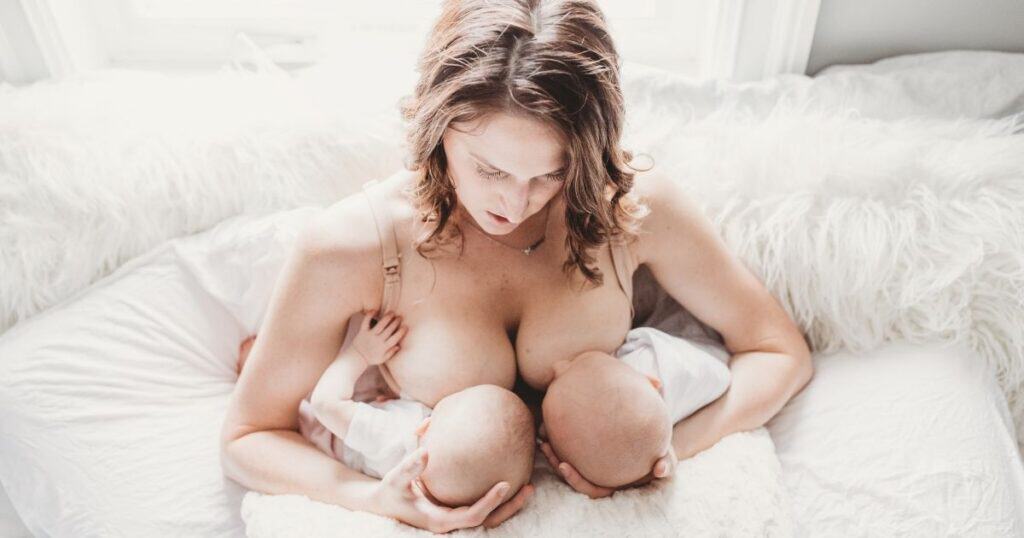 Mom sits in bed nursing twins in the football hold
