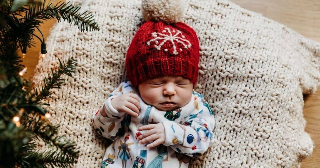 Newborn in snowflake hat lies beneath a tree