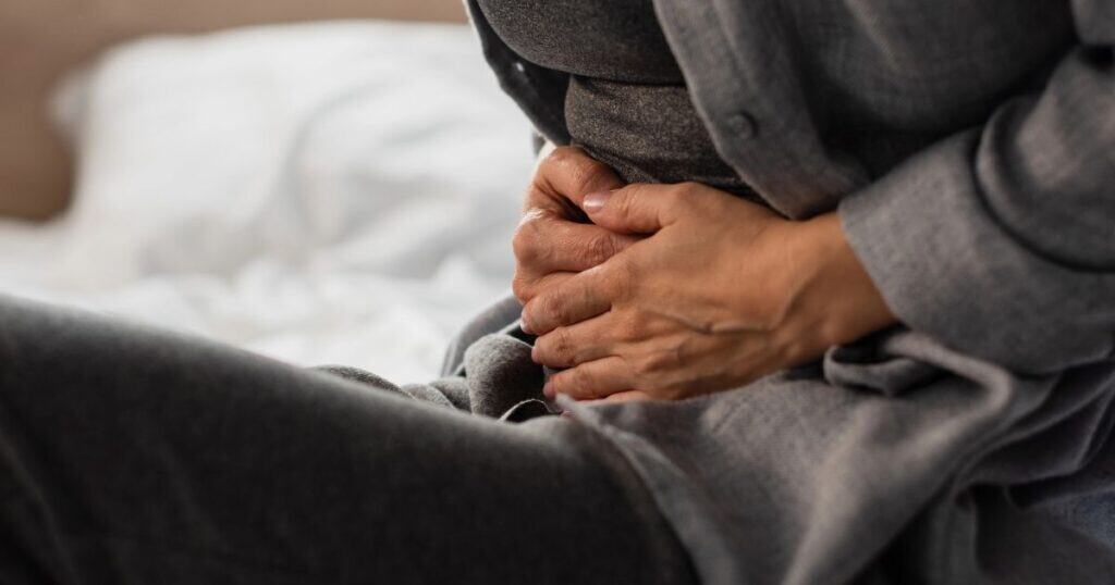 Woman sits on bed cradling abdomen