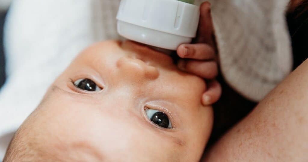 Baby drinks from bottle while looking up into camera