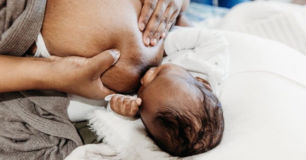Mom holds breast while baby breastfeeds in the football hold