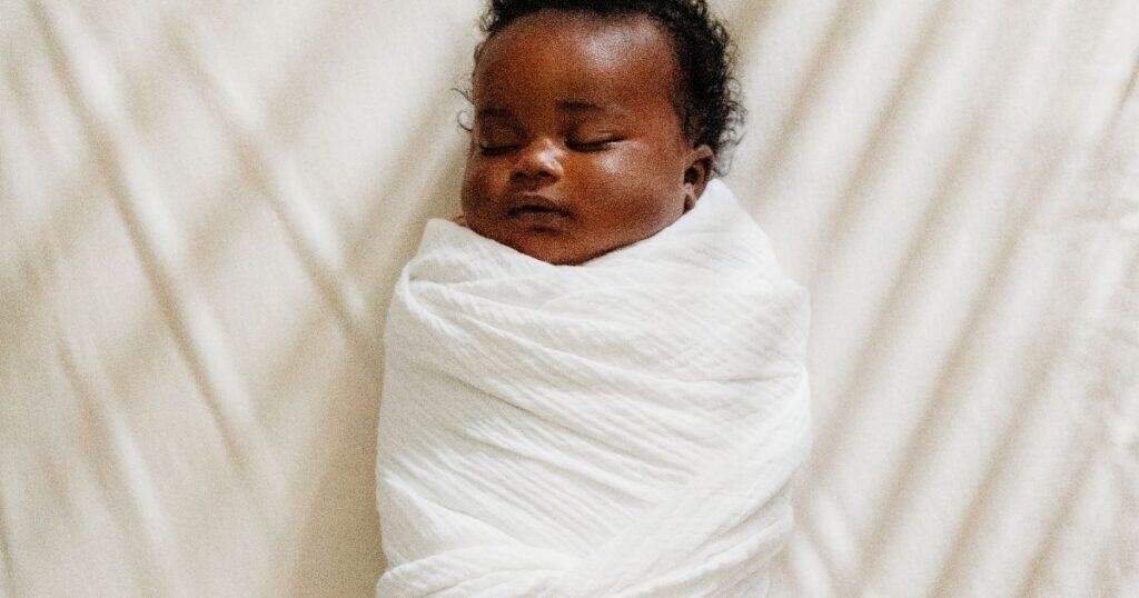 Baby in a white swaddle sleeps in crib