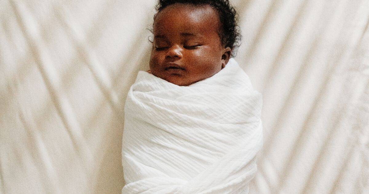 Baby in a white swaddle sleeps in crib