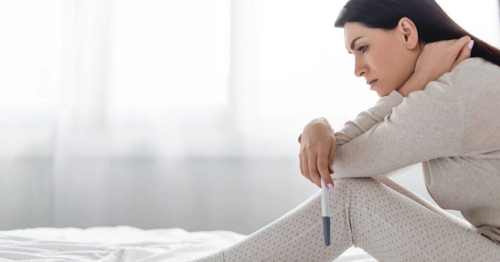 Woman sits on bed sadly