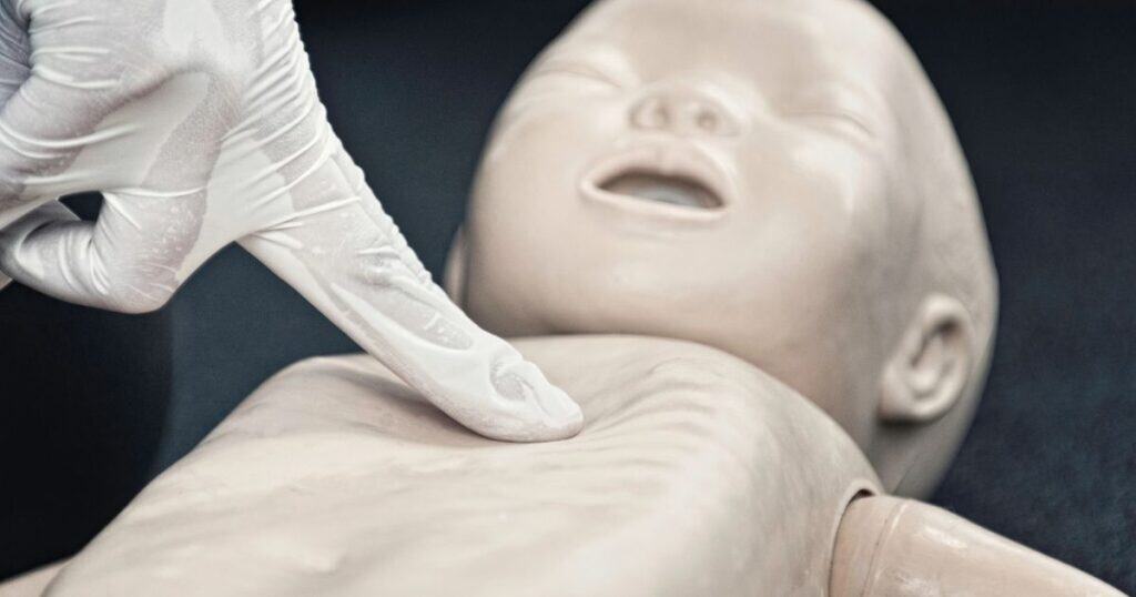 Gloved hand demonstrates chest comptessions on infant CPR dummy
