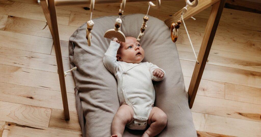 Awake baby plays on back with hanging wooden toys above them