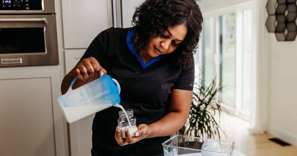 Postpartum Doula pours formula from a pitcher into a glass bottle
