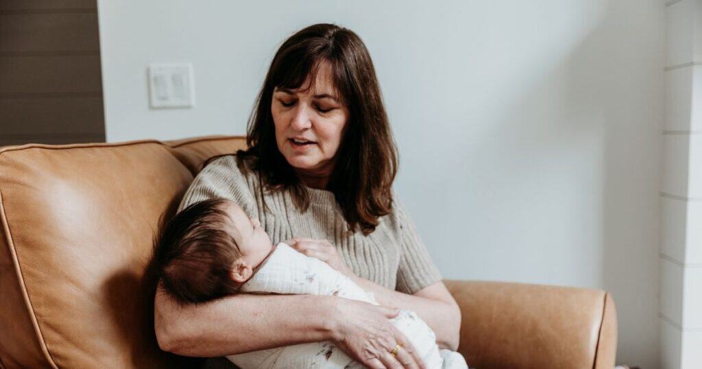 Doula sits in chair with swaddled baby and soothes them