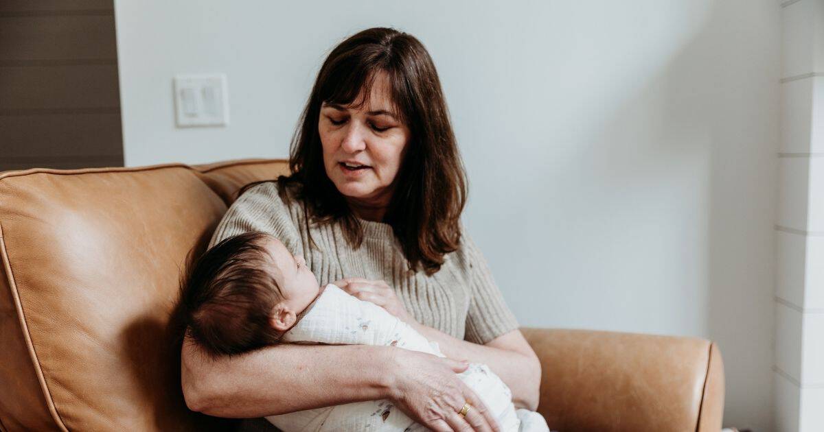Doula sits in chair with swaddled baby and soothes them