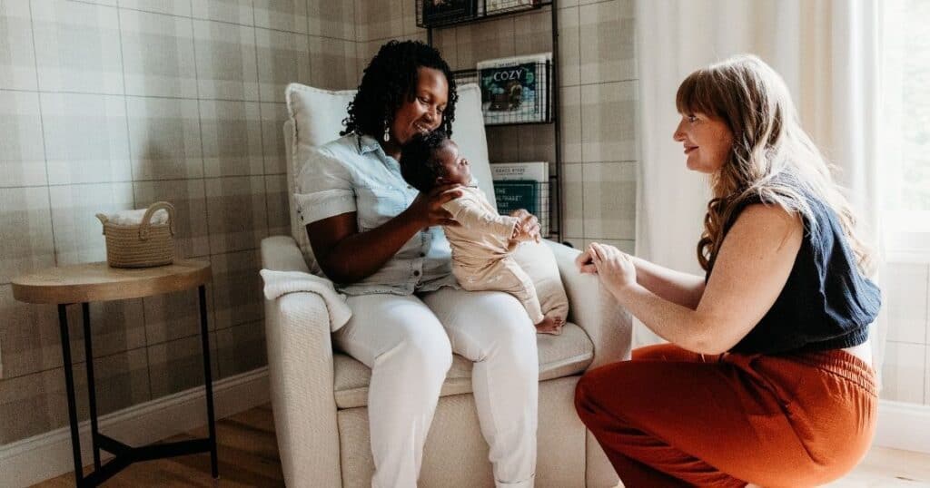 Postpartum doula crouches nect to mom and baby in recliner