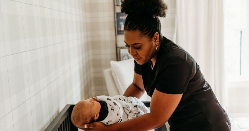 Postpartum Doula places swaddled baby to sleep in crib