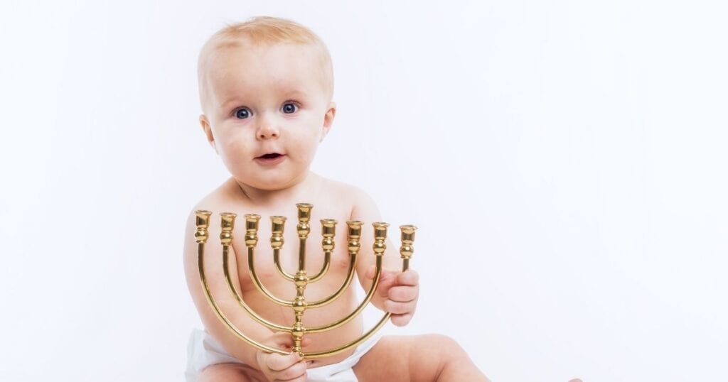 Baby sits up holding a menorah