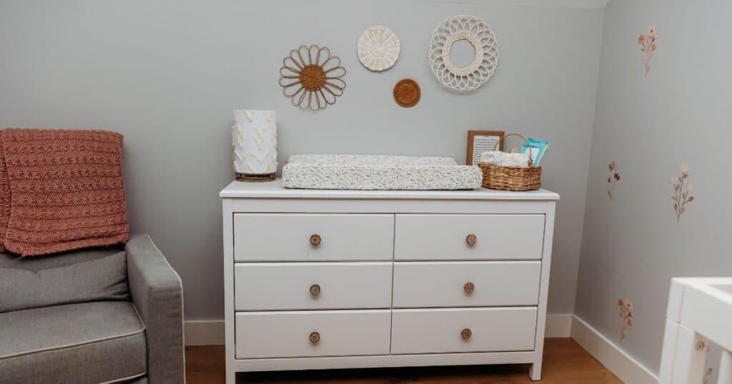 White dresser with changing pad, grey rocking chair in nursery