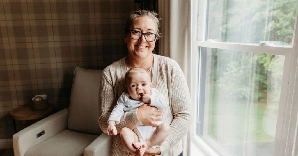Postpartum doula holds happy baby facing outward on her chest
