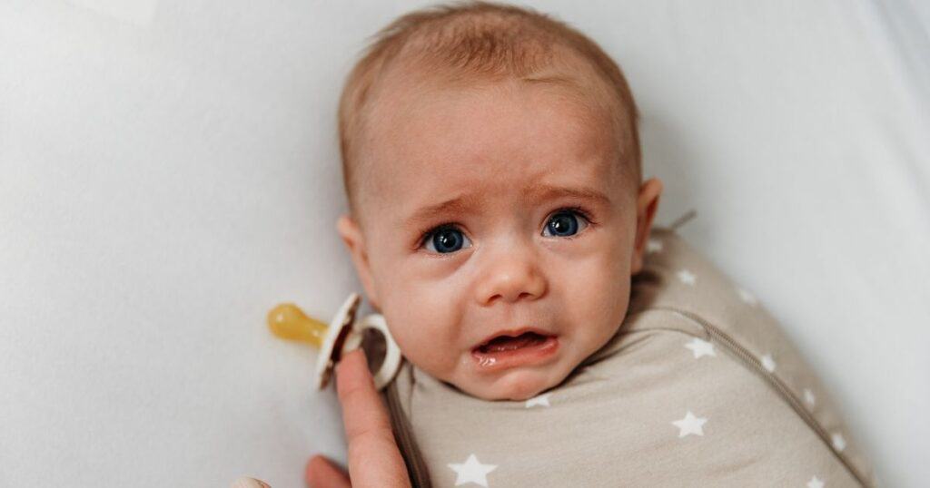 baby in swaddle in crib, mom holding pacifier