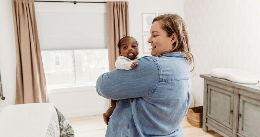 Postpartum Doula holds baby upright in nursery