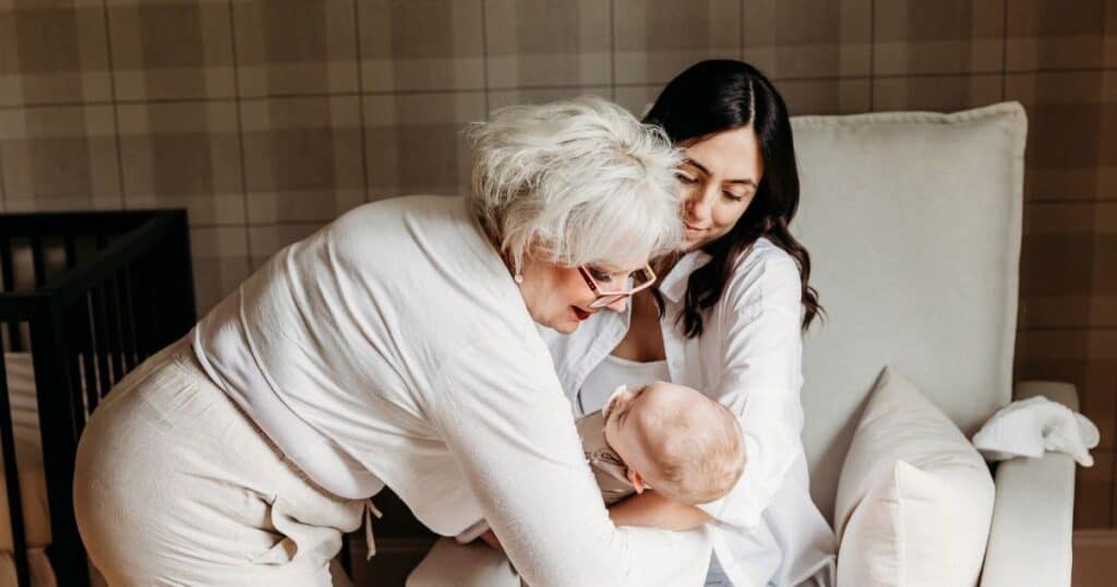 Postpartum Doula hands baby to breastfeeding mom in nursery