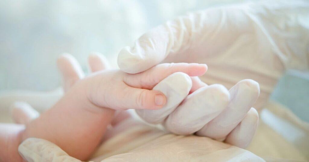 Gloved hands hold newborn hand
