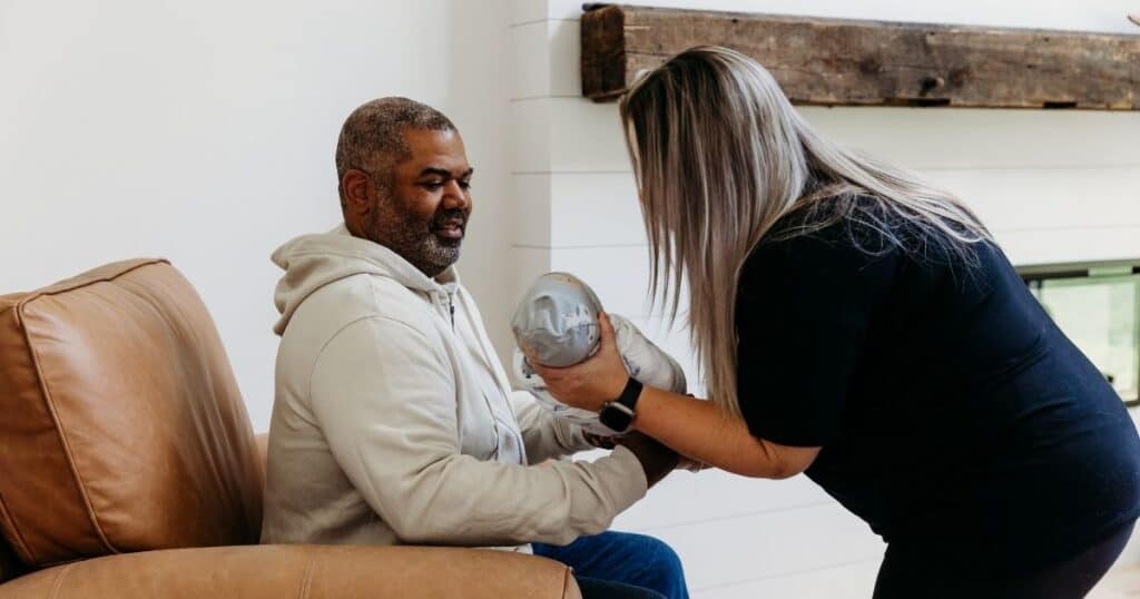 Postpartum Doula hands baby to new dad sitting in chair