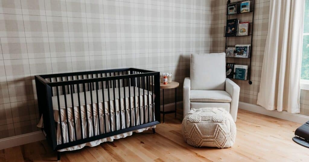 Black crib, grey rocking chair, white foot rest and tan plaid walls of a nursery