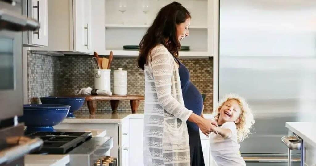 pregnant woman cooking in kitchen with toddler for postpartum meal prep