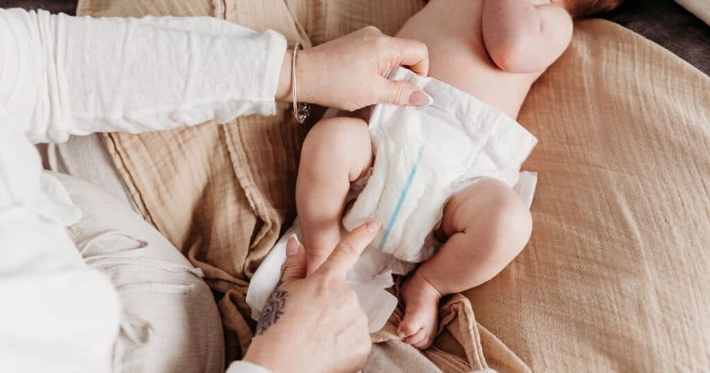 Baby with wet diaper gets diaper change from Postpartum Doula with tattooed hand