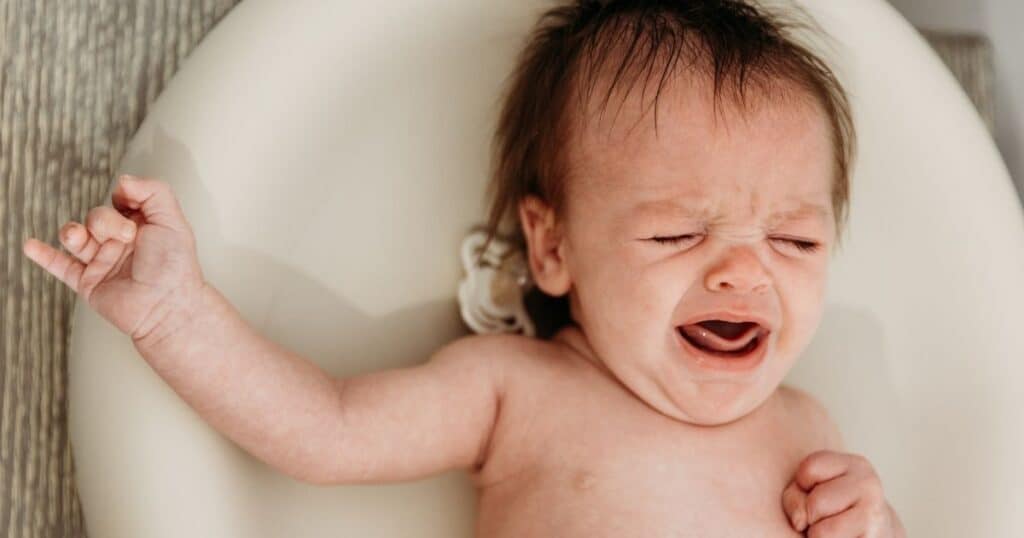 Baby crying on changing table with pacifier next to their ear