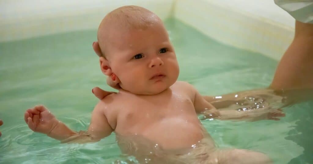 Baby swims on back in water supported by mothers hands