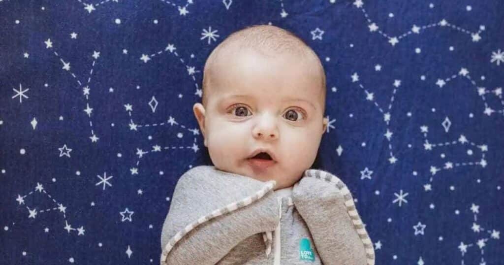 Surprised baby laying on blue blanket.