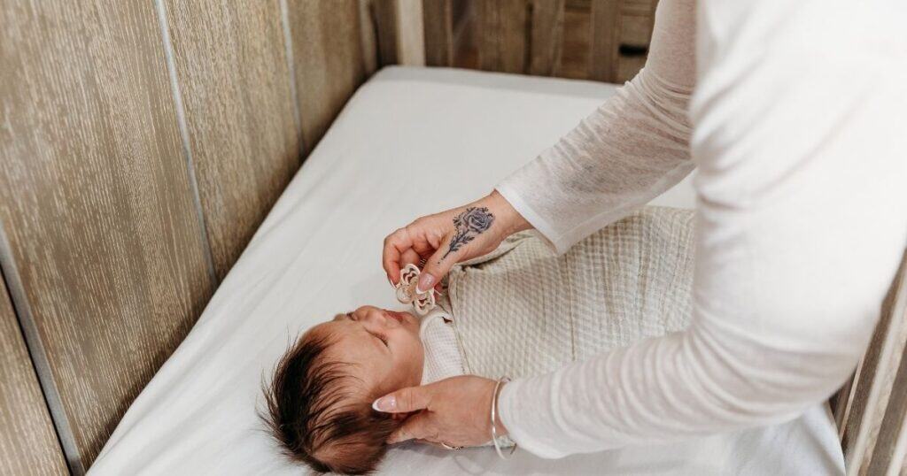 Newborn Care Specialist with rose tattoo on her hand offeres pacifier to fussy, swaddled baby to help soothe them