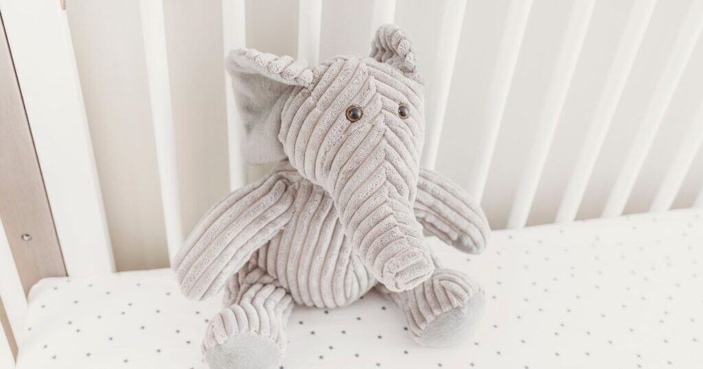 Elephant stuffed animal sits against crib bars