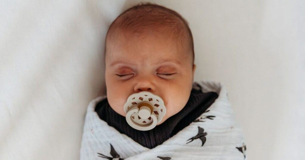 Sleeping baby with tan pacifier and bird swadd;e