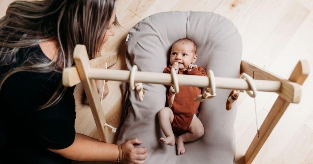 Doula sits on floor with baby who is playing on back
