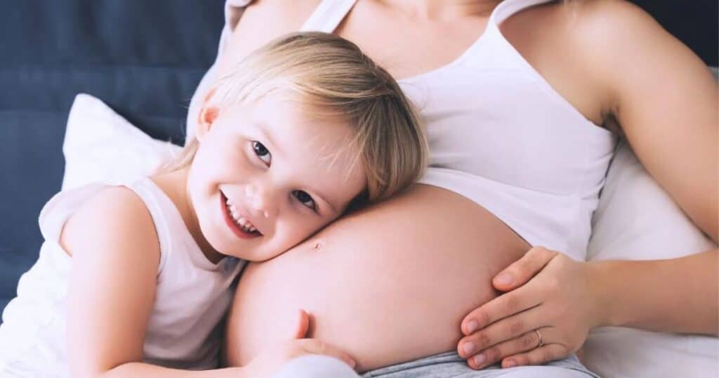 Mom with child laying their head on her pregnant belly.