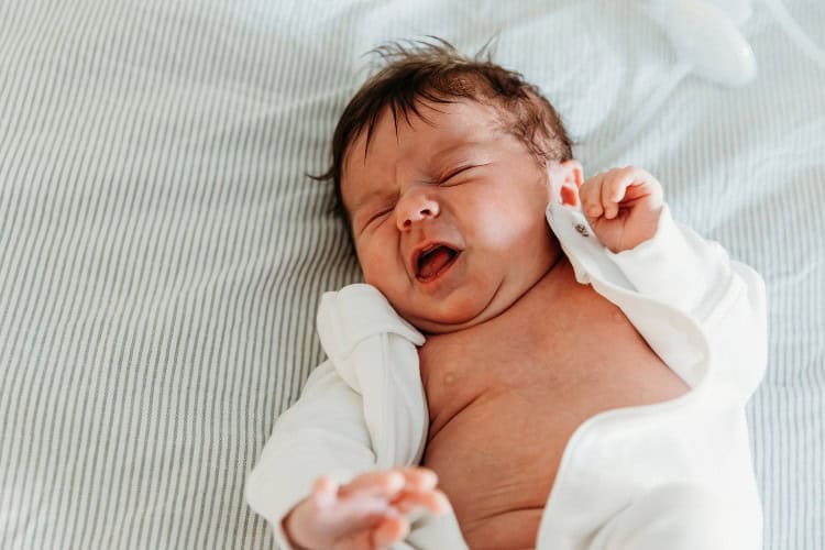 Newborn in bed yawning as a sleep cue