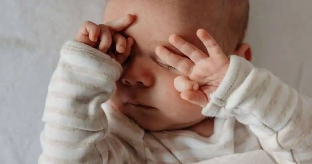 Sleepy baby with hands on their face.