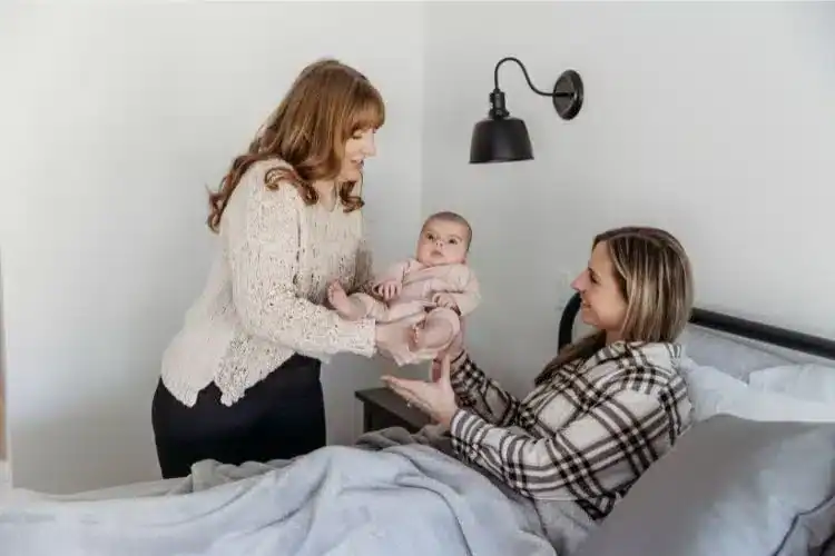 Postpartum doula hands newborn baby to new mom in bed