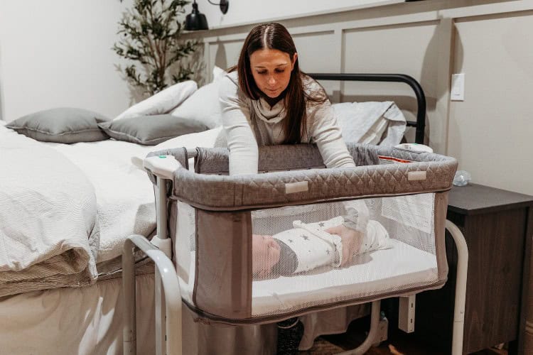 new mom placing baby in crib by bed