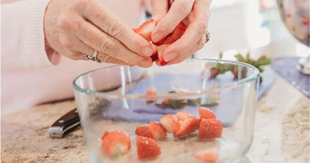 hands holding strawberries over a bowl