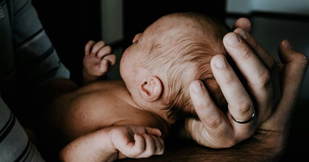 newborn head cradled in parents hand