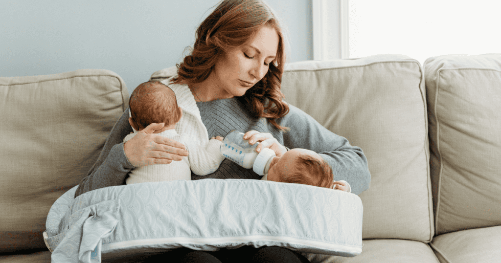 A newborn care specialist feeding two babies on a feeding pillow