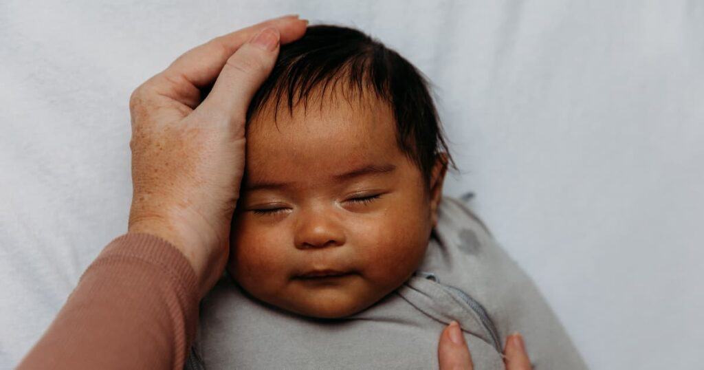 Newborn Care Specialist from Well Supported Family soothing a swaddled baby to sleep by stroking their face.